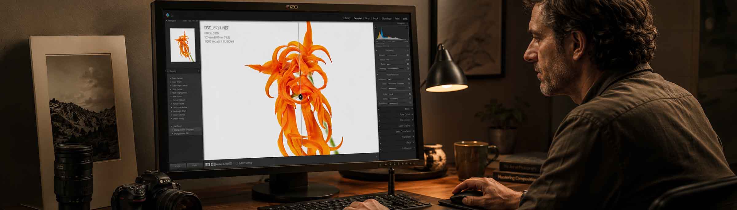 Ein Fotograf bearbeitet ein Foto einer leuchtend orangefarbenen Blume auf einem Computerbildschirm, während eine Kamera und ein Objektiv auf dem Schreibtisch stehen.