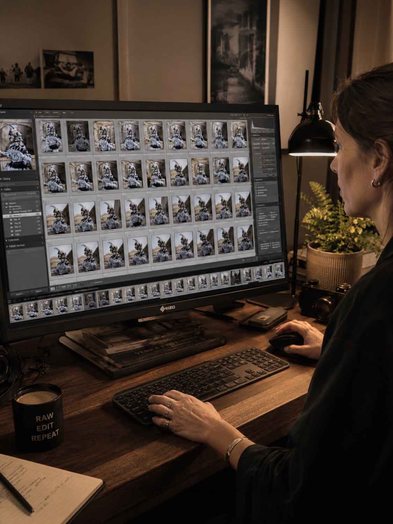Eine Person sitzt an einem Schreibtisch und bearbeitet mehrere RAW-Arbeitsablauf-Fotos eines Hundes auf einem großen Computermonitor. In der Nähe befinden sich eine Tasse, ein Notebook, eine Tastatur und eine Pflanze in einem warm beleuchteten Raum.