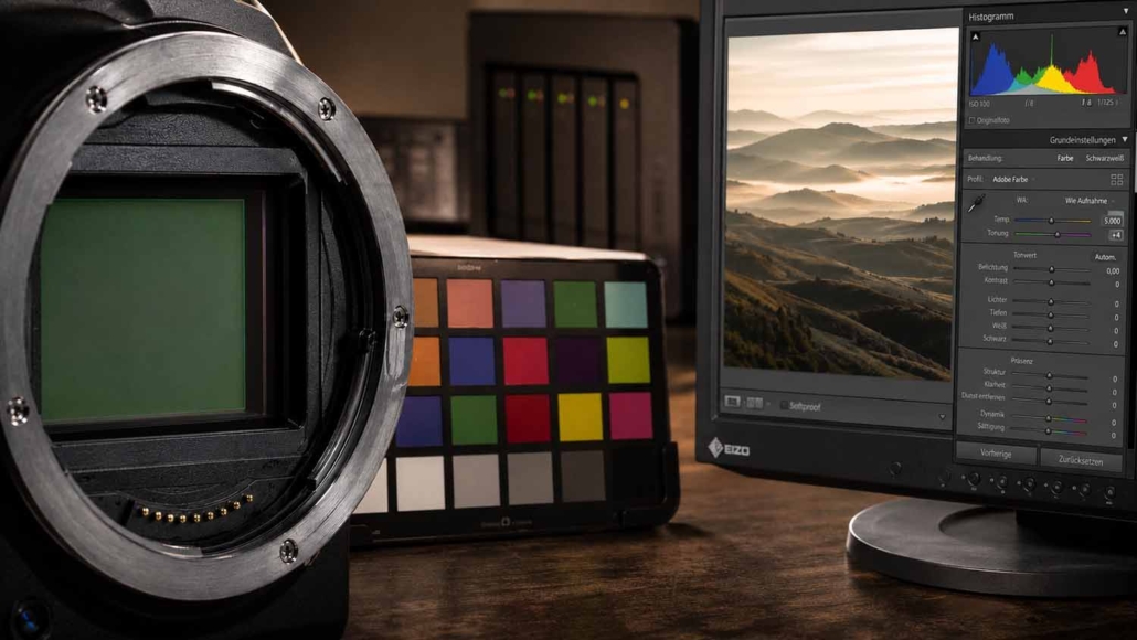 Nahaufnahme eines Kamerasensors, eines Farbkalibrierungsdiagramms und eines Computermonitors, auf dem die Bildbearbeitungssoftware Lightroom Workshop mit einem Landschaftsbild und einem Histogramm angezeigt wird.