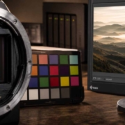 Nahaufnahme eines Kamerasensors, eines Farbkalibrierungsdiagramms und eines Computermonitors, auf dem die Bildbearbeitungssoftware Lightroom Workshop mit einem Landschaftsbild und einem Histogramm angezeigt wird.