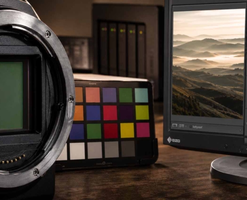 Nahaufnahme eines Kamerasensors, eines Farbkalibrierungsdiagramms und eines Computermonitors, auf dem die Bildbearbeitungssoftware Lightroom Workshop mit einem Landschaftsbild und einem Histogramm angezeigt wird.