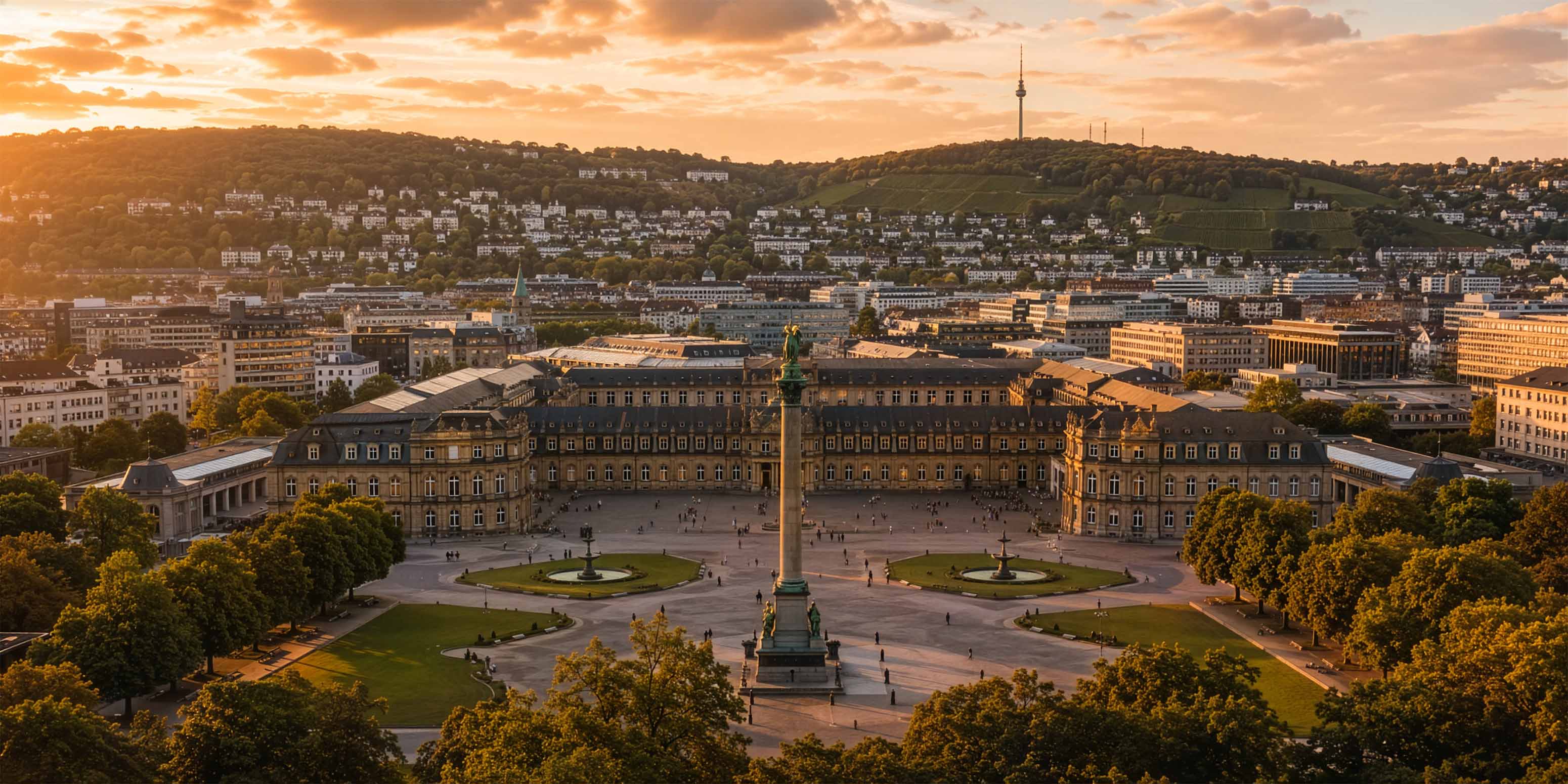 Luftaufnahme des Stuttgarter Schlossplatzes bei Sonnenuntergang. Zu sehen sind das Neue Schloss, die Mittelsäule, baumgesäumte Wege und städtische Gebäude mit grünen Hügeln - eine inspirierende Szene für jeden Bildbearbeitung Workshop Stuttgart - unter einem teilweise bewölkten Himmel.