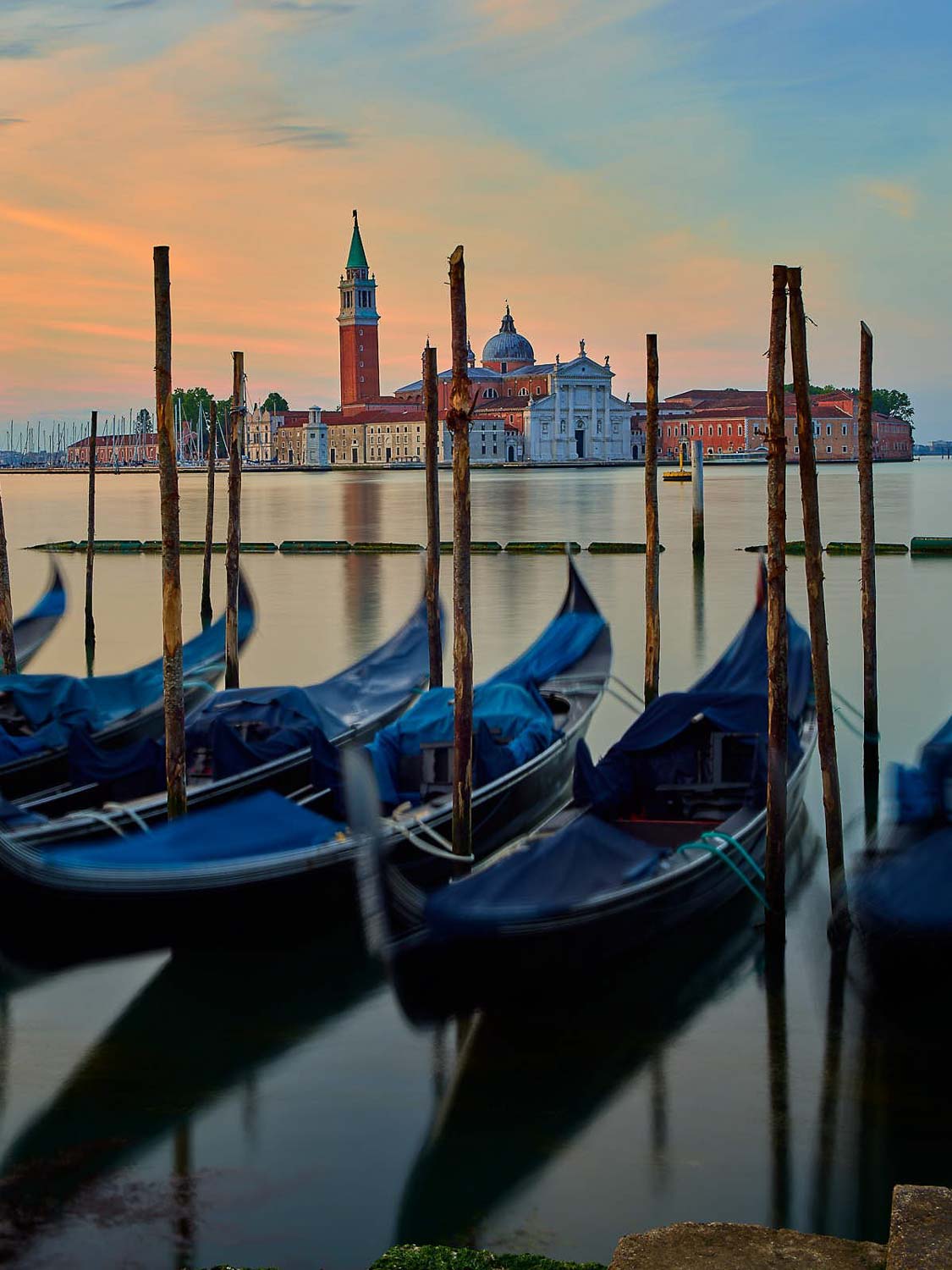Bei Sonnenuntergang liegen mehrere Gondeln auf dem ruhigen Wasser vor dem Hintergrund der historischen Insel San Giorgio Maggiore und ihrer Kirche in Venedig, Italien.